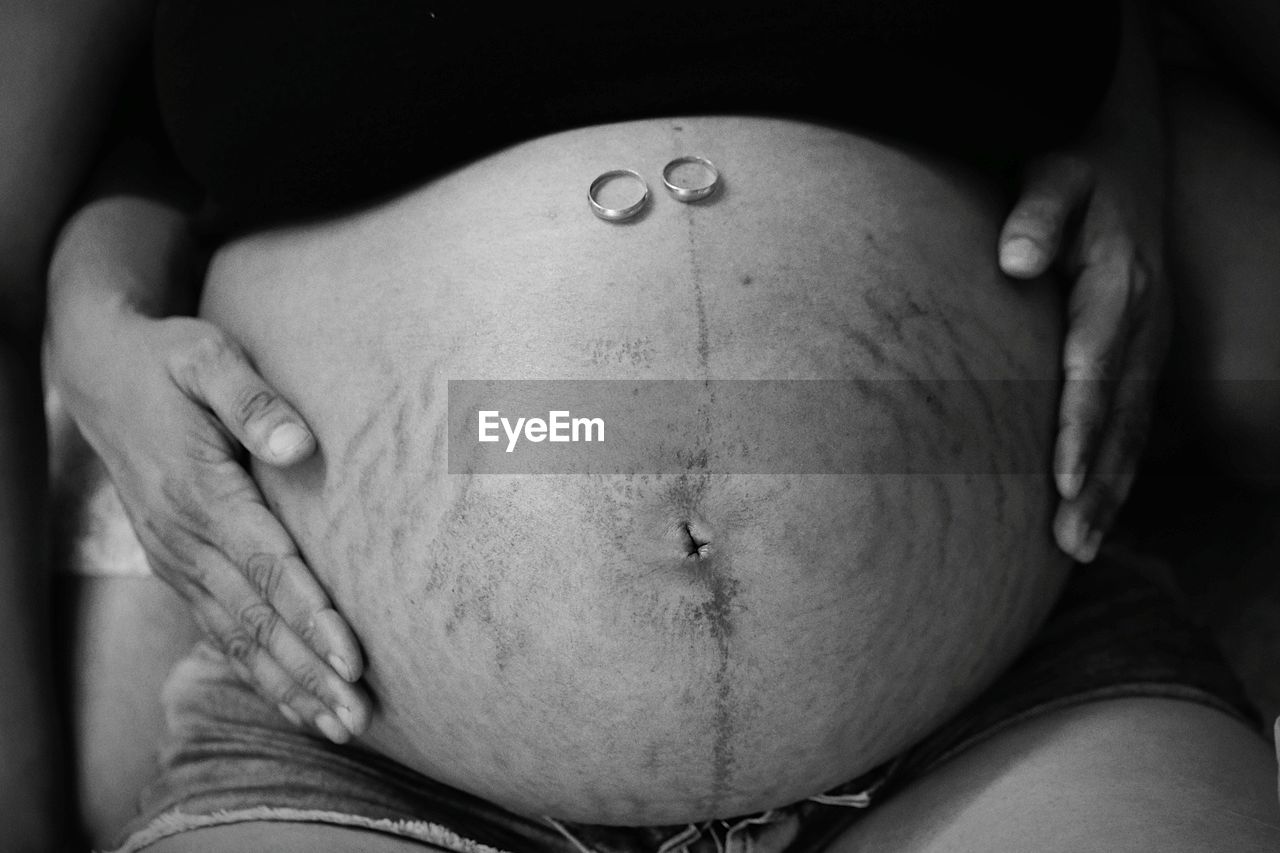 Midsection of pregnant woman with wedding rings on stomach