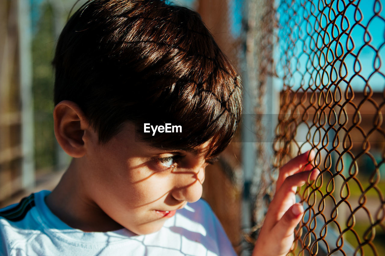 Close-up portrait of boy looking through fence