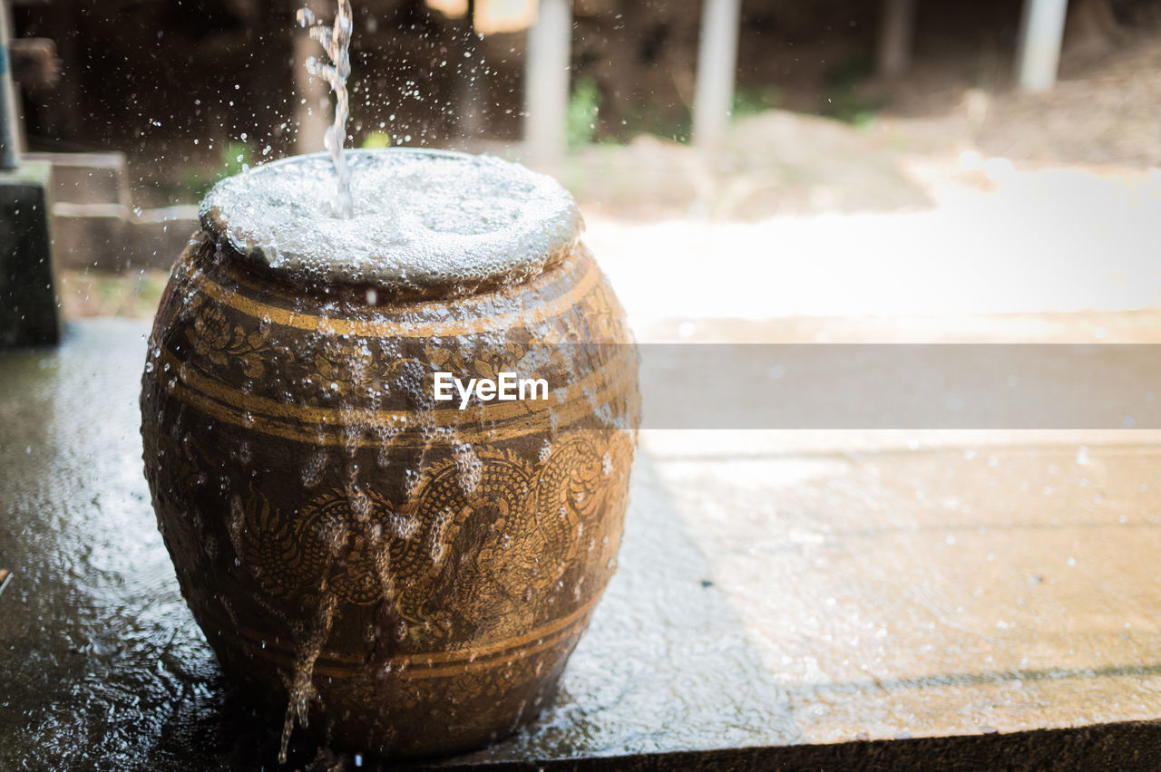 High angle close-up of water flowing from jar on wooden tables