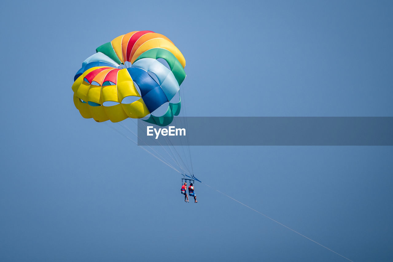 Low angle view of people paragliding against sky