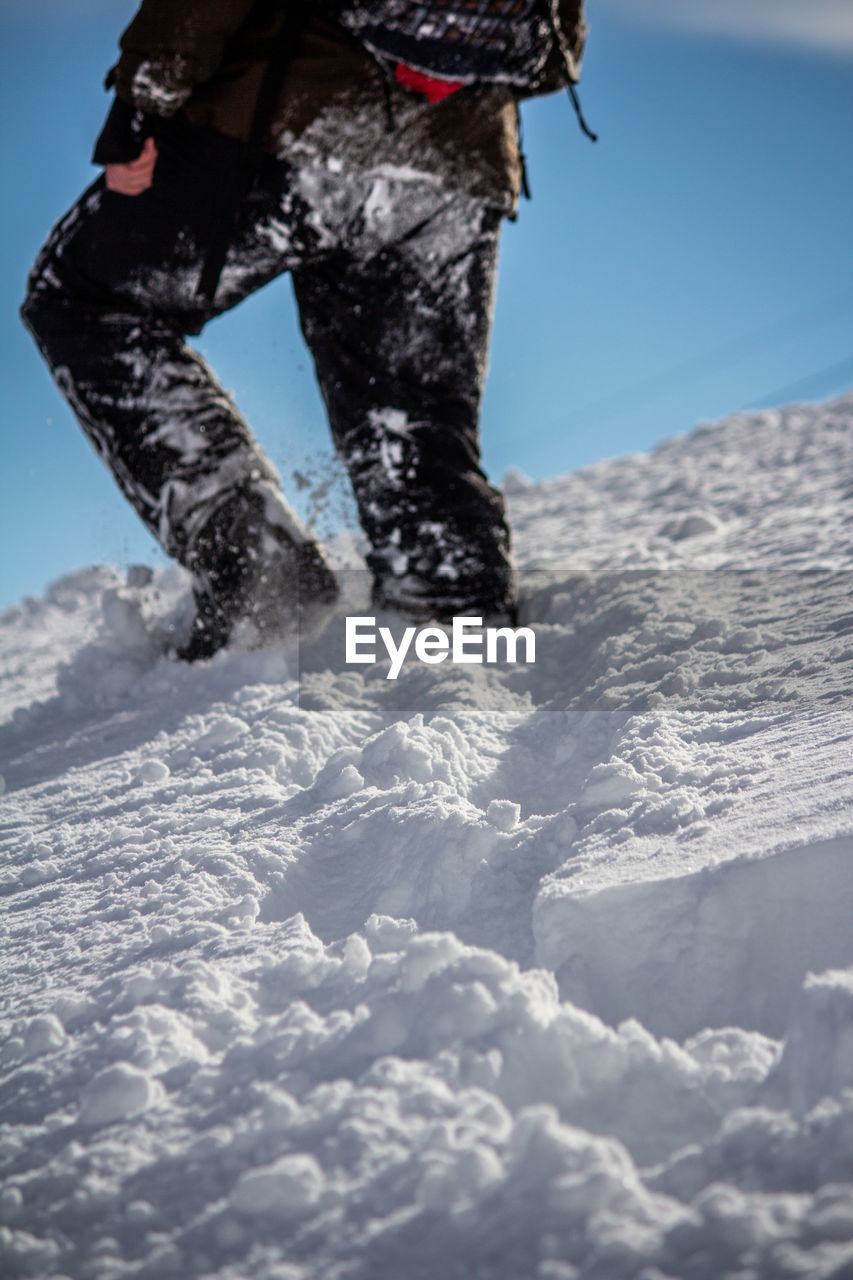 Low section of person walking on snowcapped mountain against sky