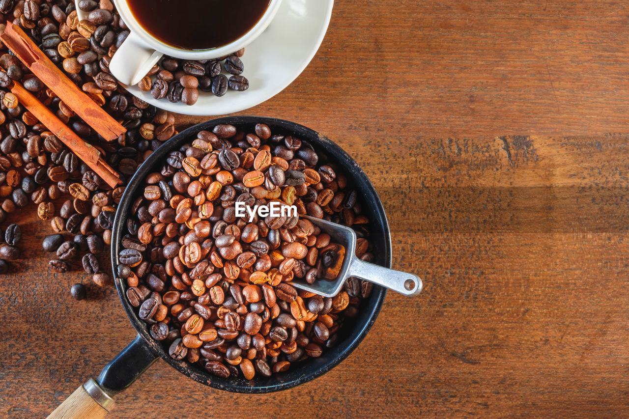 food and drink, coffee, food, drink, cup, coffee cup, mug, roasted coffee bean, table, refreshment, kitchen utensil, high angle view, brown, freshness, wood, no people, hot drink, spoon, crockery, produce, eating utensil, still life, directly above, indoors, saucer, healthy eating, sweet food