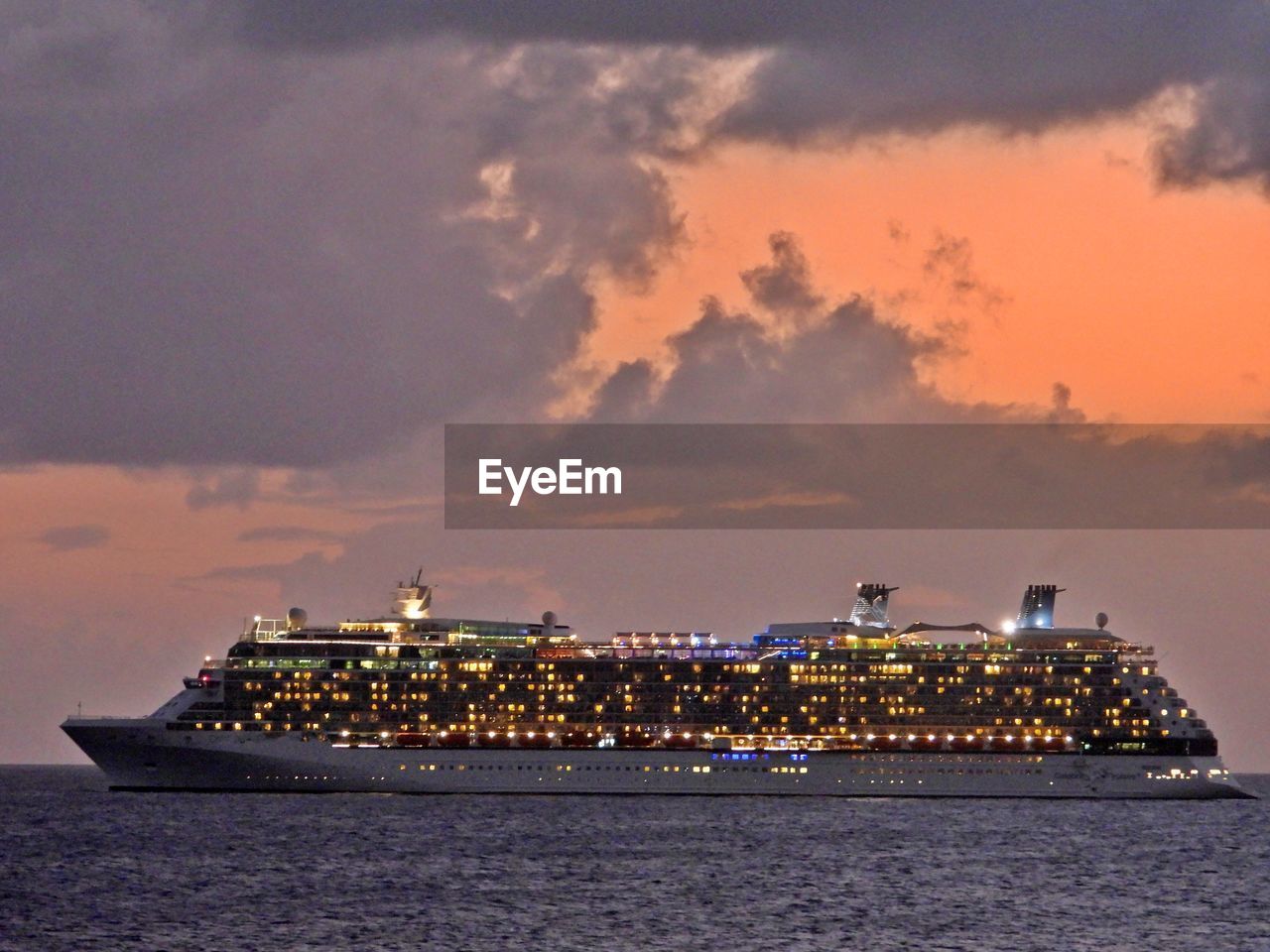 SEA BY ILLUMINATED CITYSCAPE AGAINST SKY DURING SUNSET