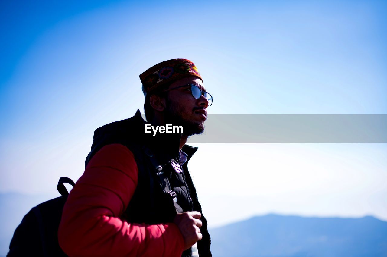 SIDE VIEW OF MAN LOOKING AWAY AGAINST BLUE SKY