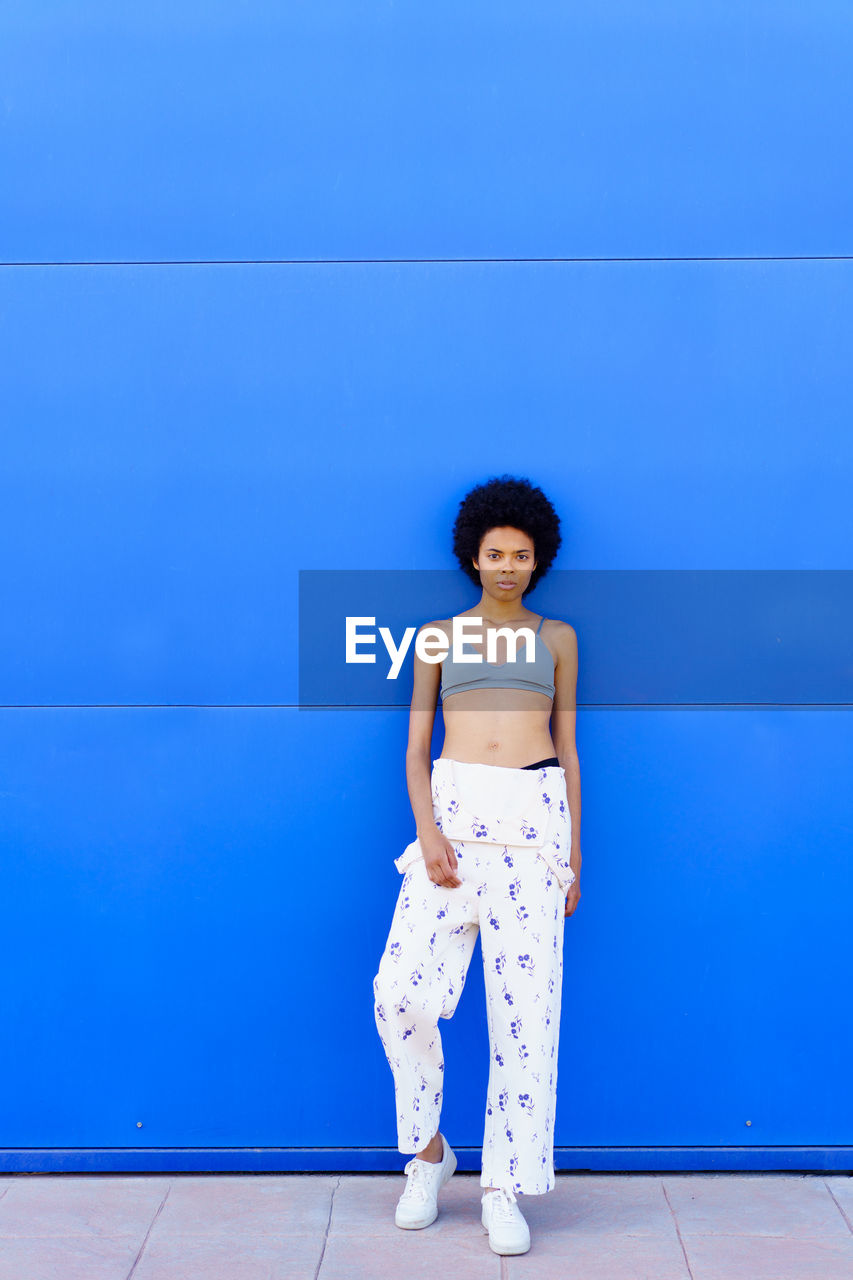 portrait of young woman standing against blue wall