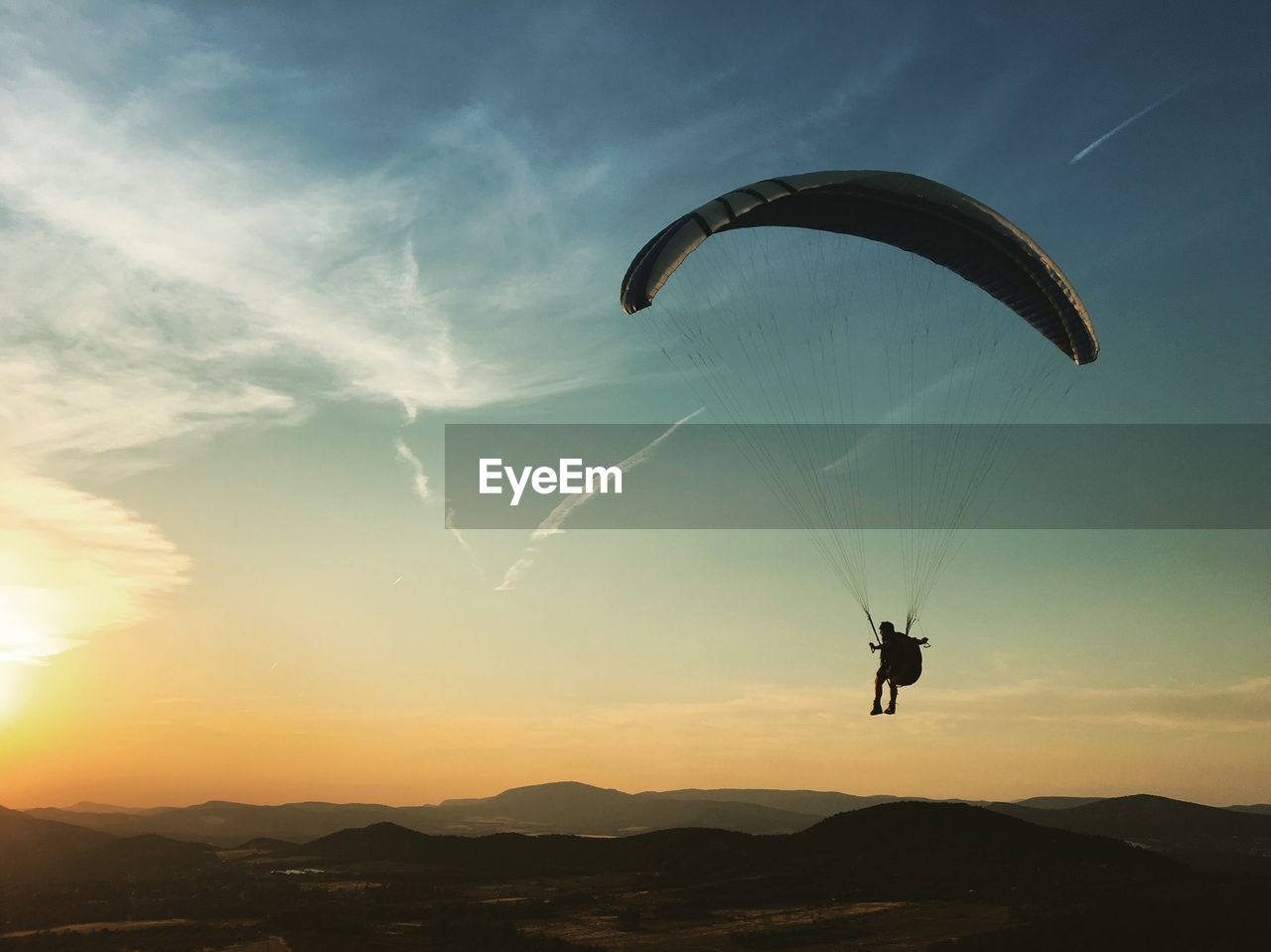 Silhouette man paragliding against sky during sunset