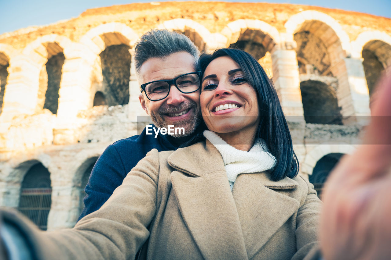 Portrait of couple doing selfie while standing against historical building