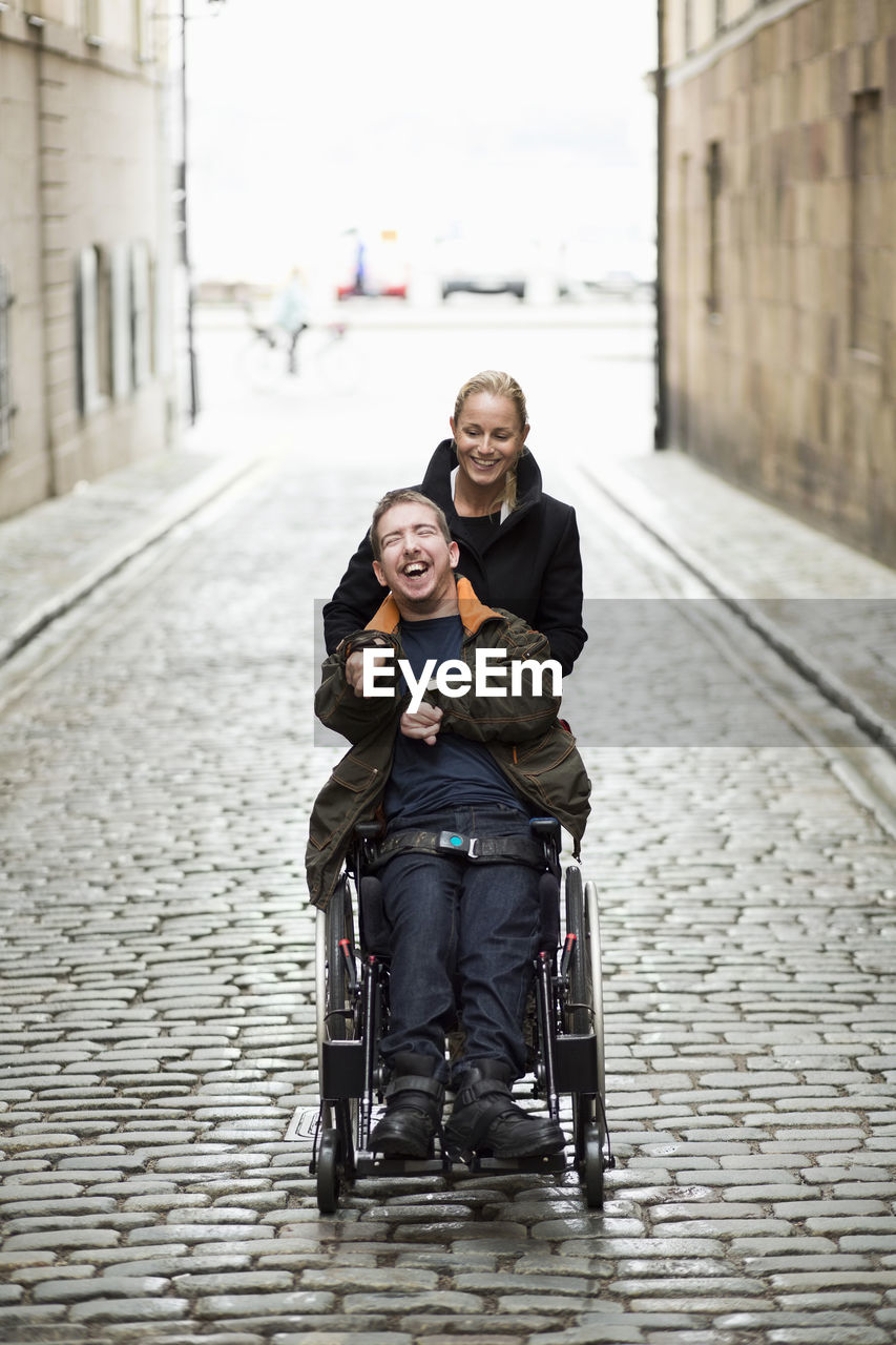 Caretaker pushing disabled man on wheelchair at city street