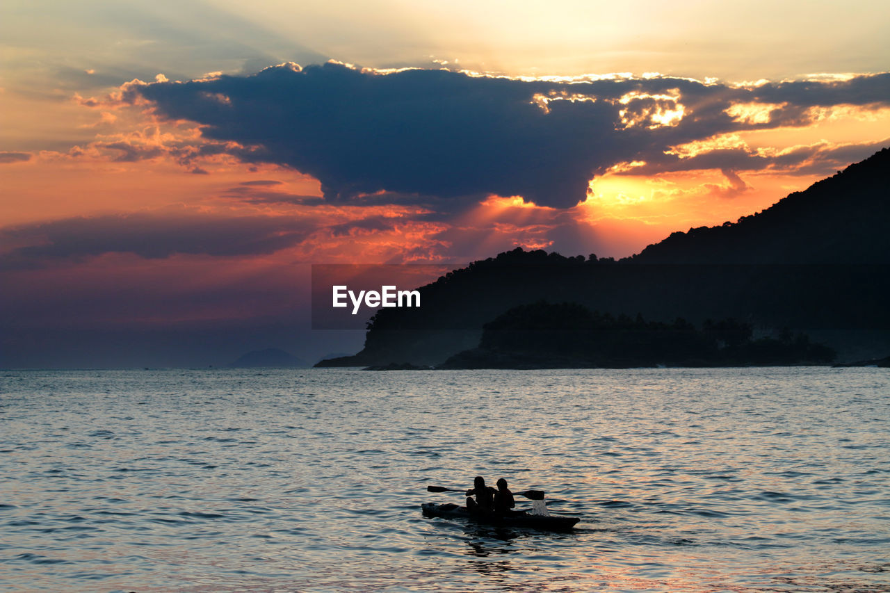 Silhouette men in boat on sea against sky during sunset