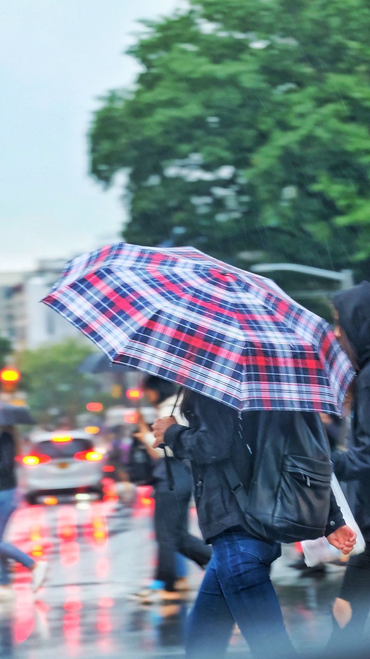 Side view of woman with umbrella walking on street during rainfall