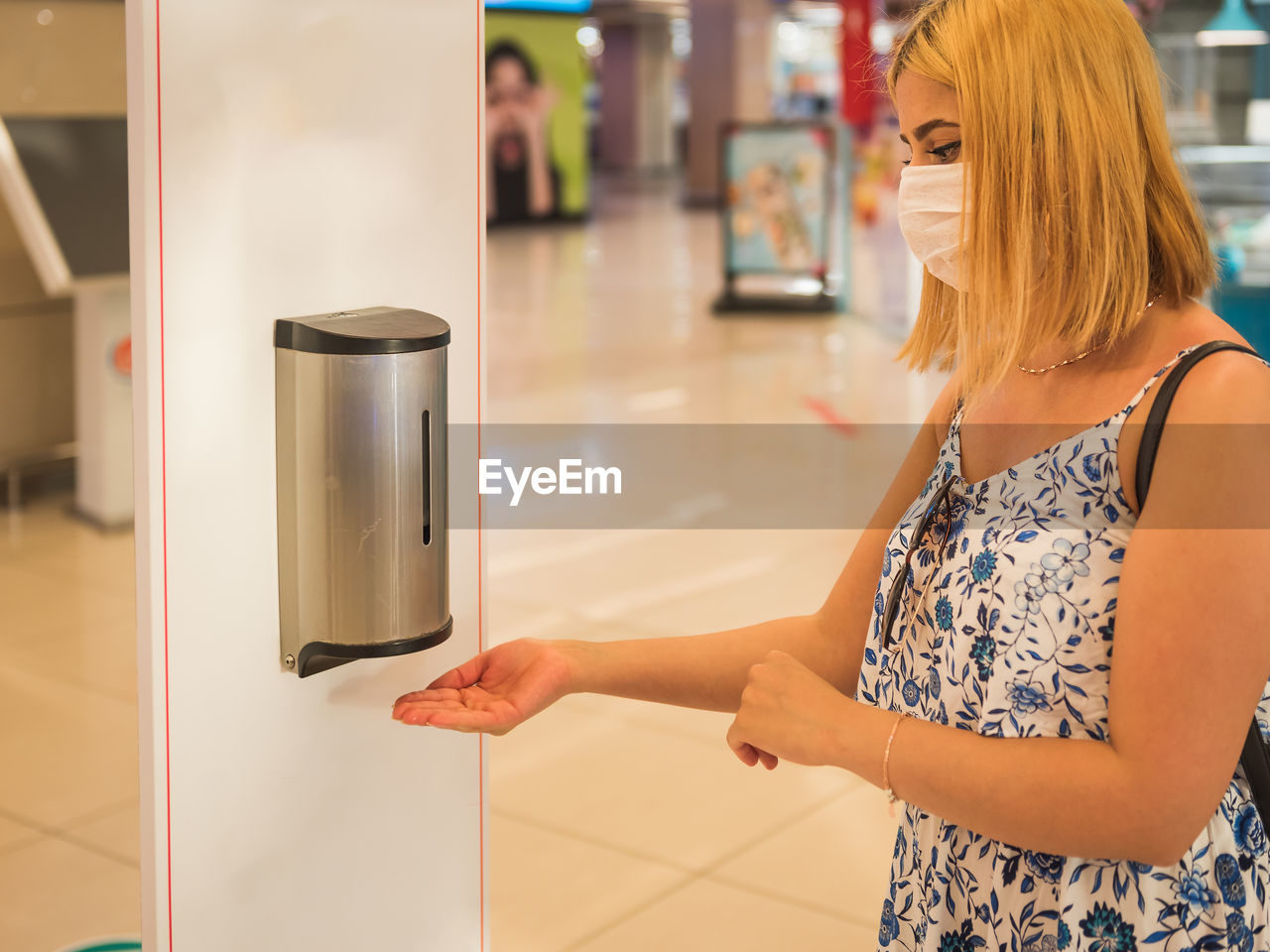 Woman wearing mask using hand sanitizer at mall