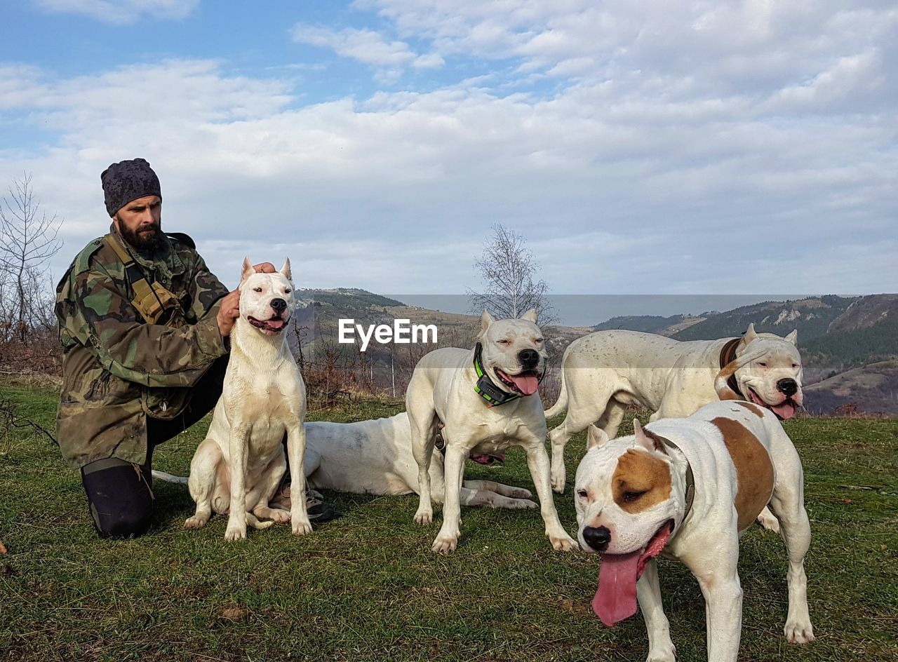 Military man with dogs on field against sky