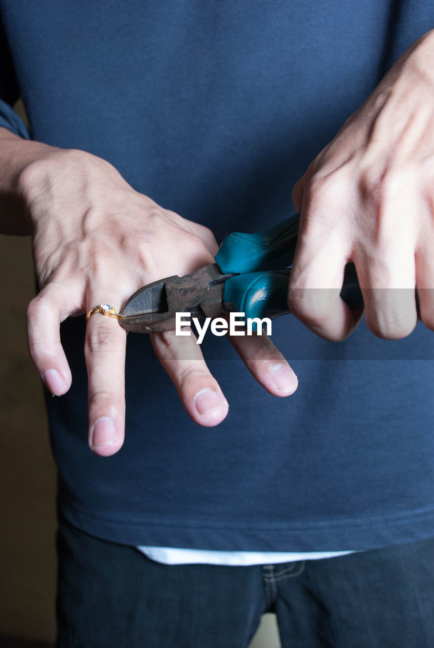 Midsection of man removing wedding ring with hand tool