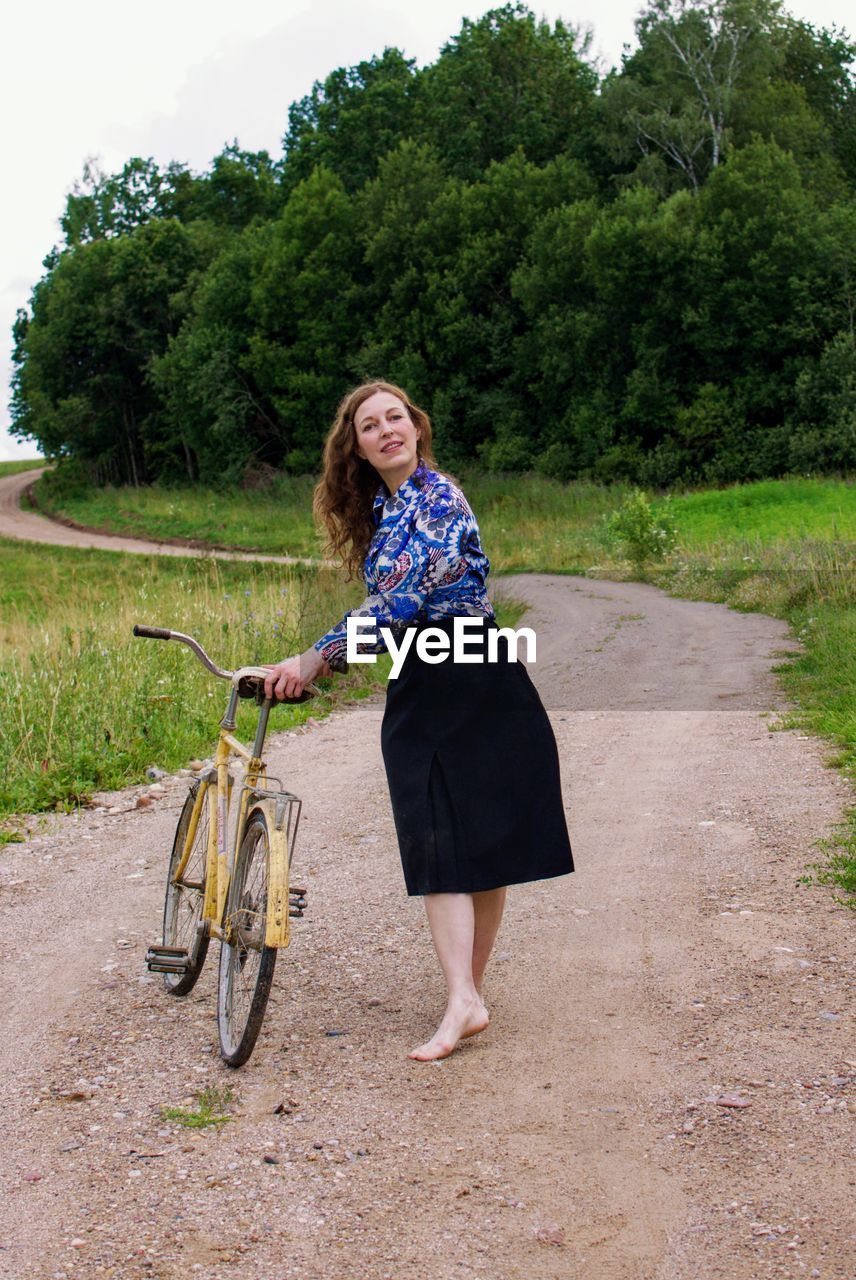 Full length of woman with bicycle on dirt road