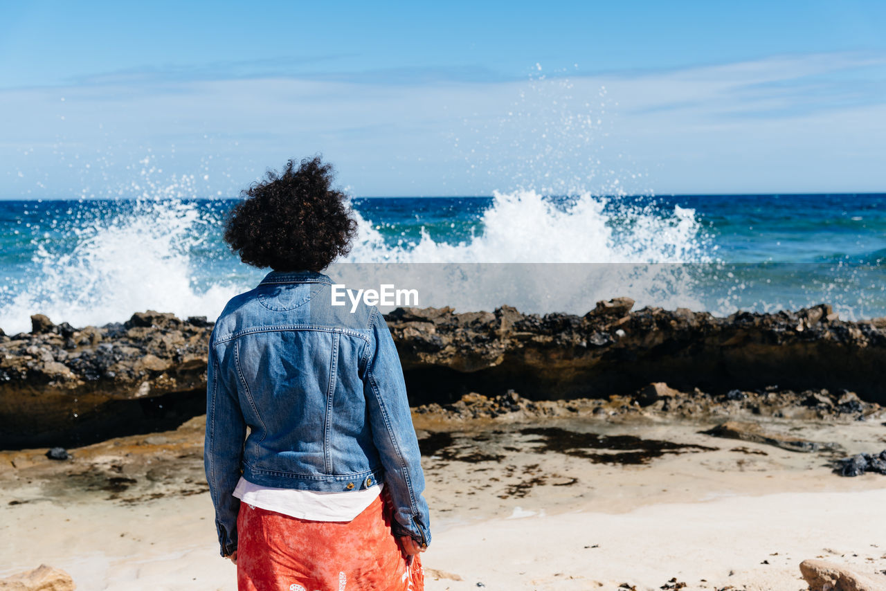 Rear view of woman standing at beach against sky