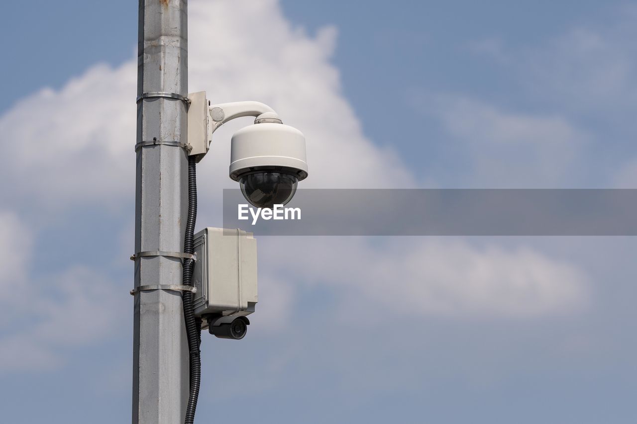 Low angle view of security camera against cloudy sky during sunny day