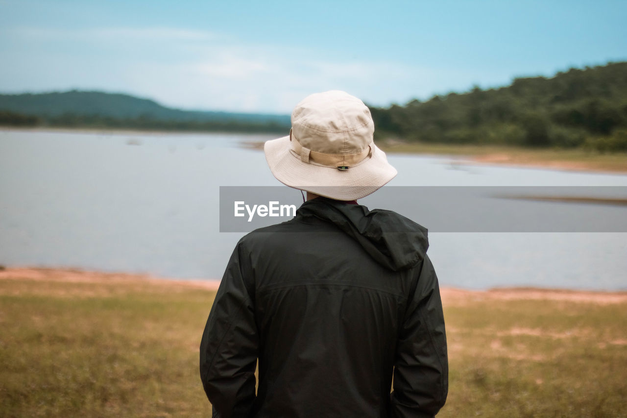 Rear view of man standing on field by lake against sky