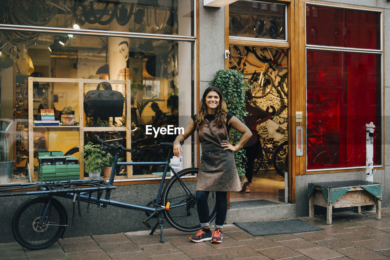 Smiling female owner standing by bicycle outside repair shop