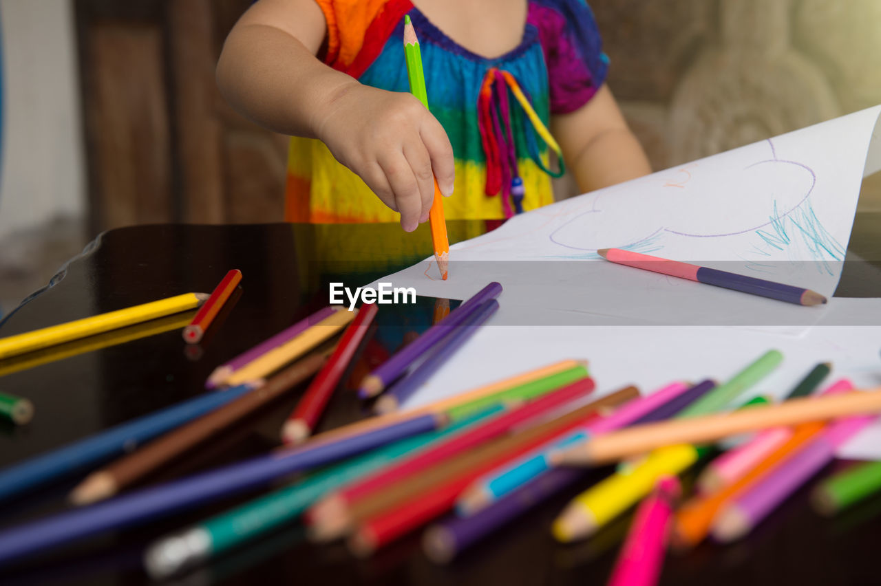 LOW SECTION OF WOMAN HOLDING PENCILS ON PAPER