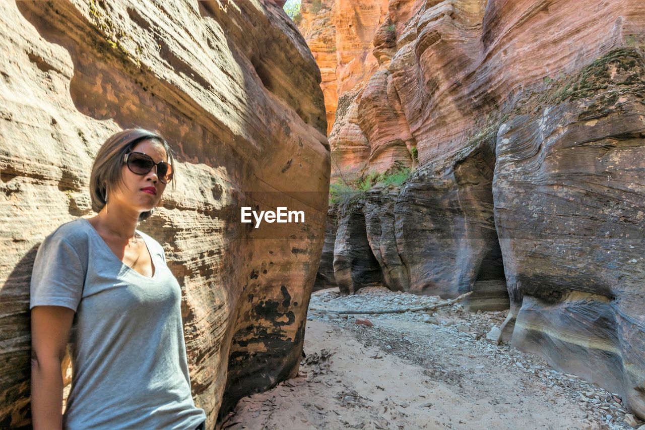 Woman wearing sunglasses standing by rock formation