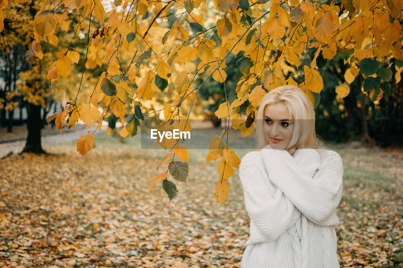 Beautiful blonde woman with autumn leaves on fall nature background. alone brooding woman in white 