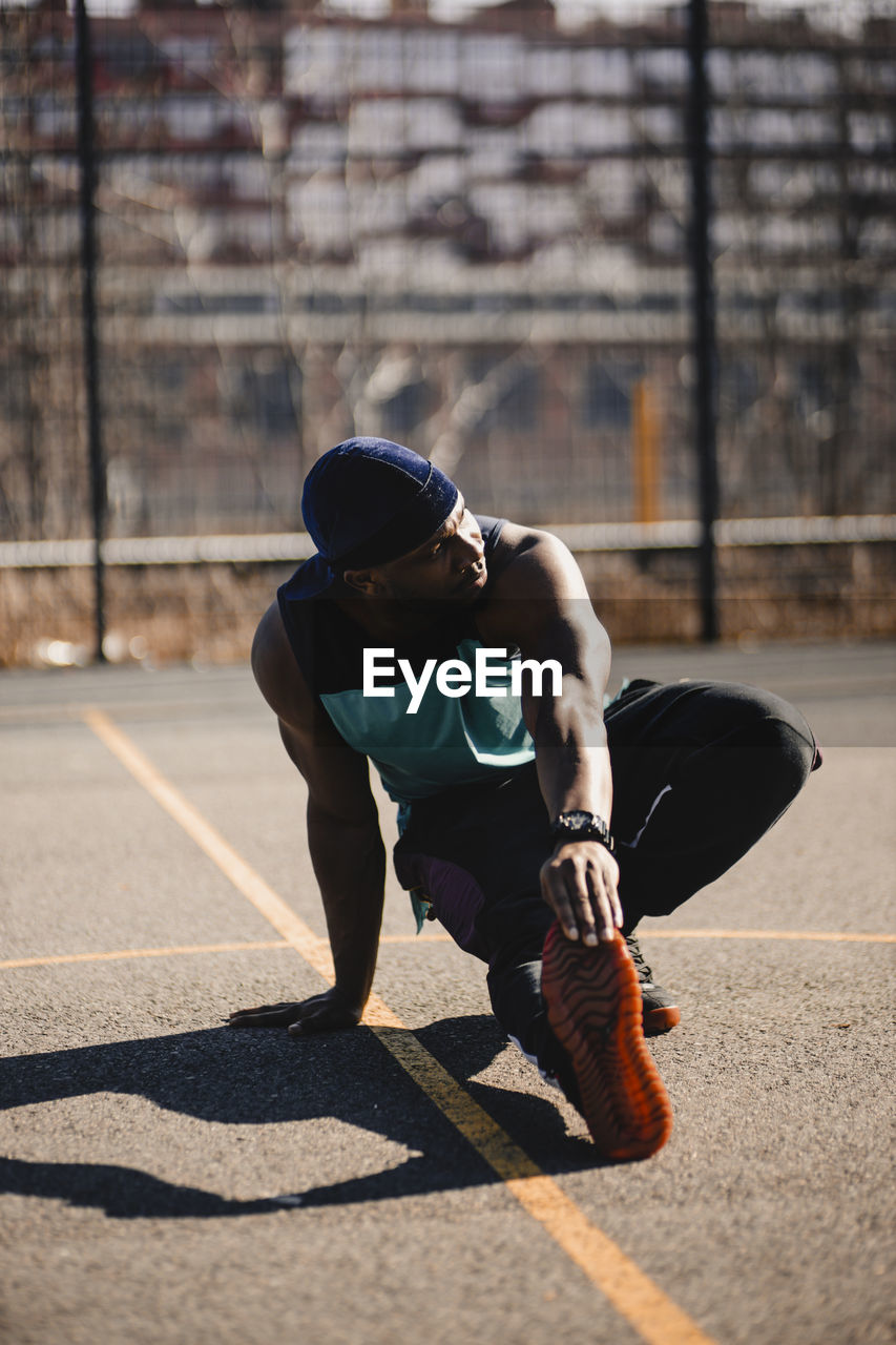 Young man stretching hand on basketball court during sunny day