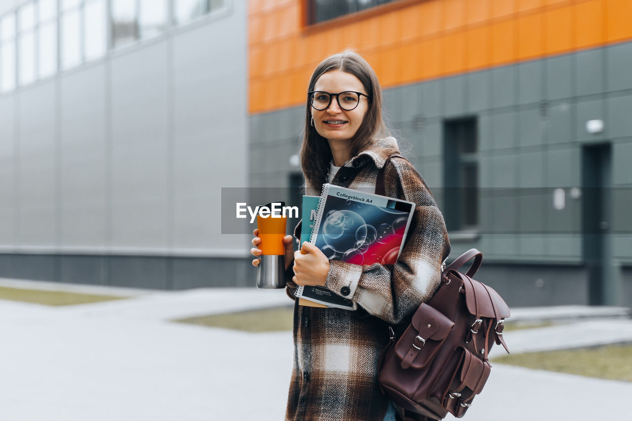 PORTRAIT OF WOMAN STANDING IN FRONT OF BUILDING