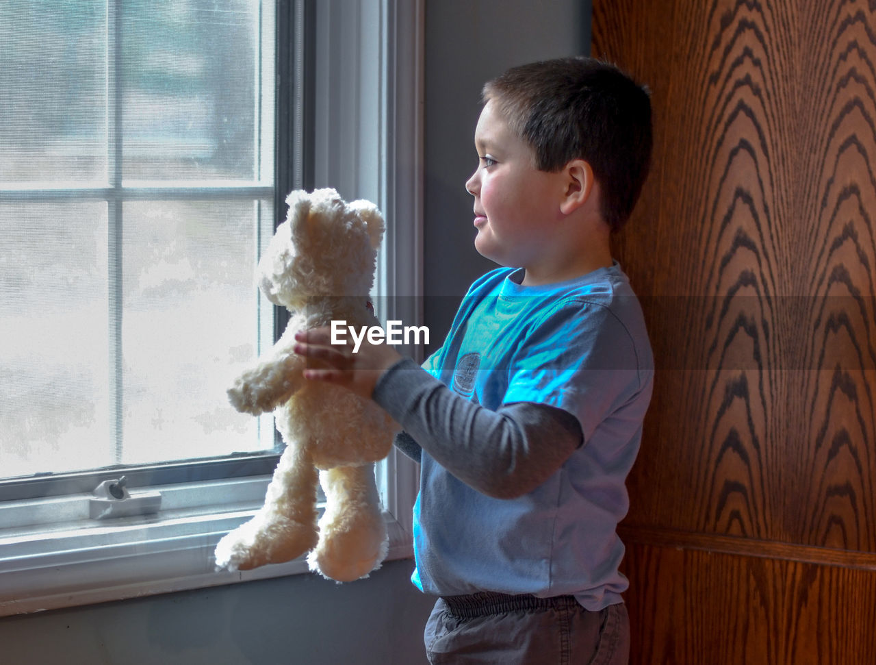 A young boy with his stuffed bear, shows the toy what is happening outside