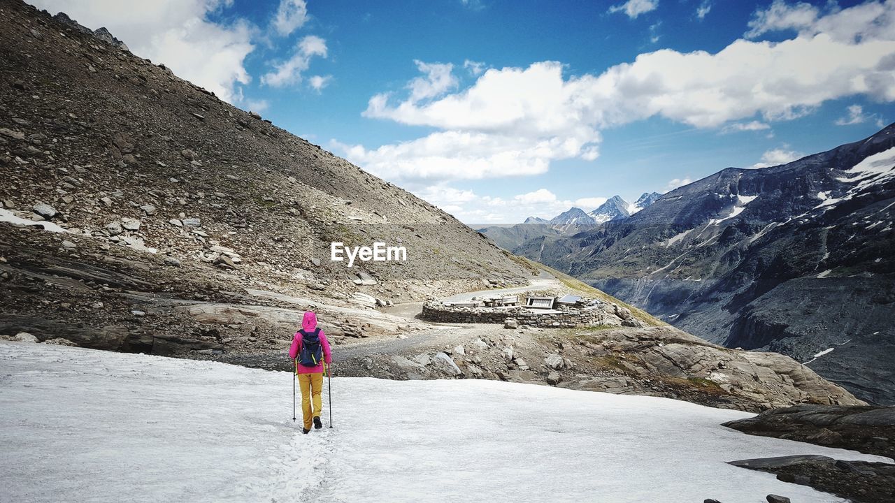 Rear view of woman walking on snowcapped mountain against sky