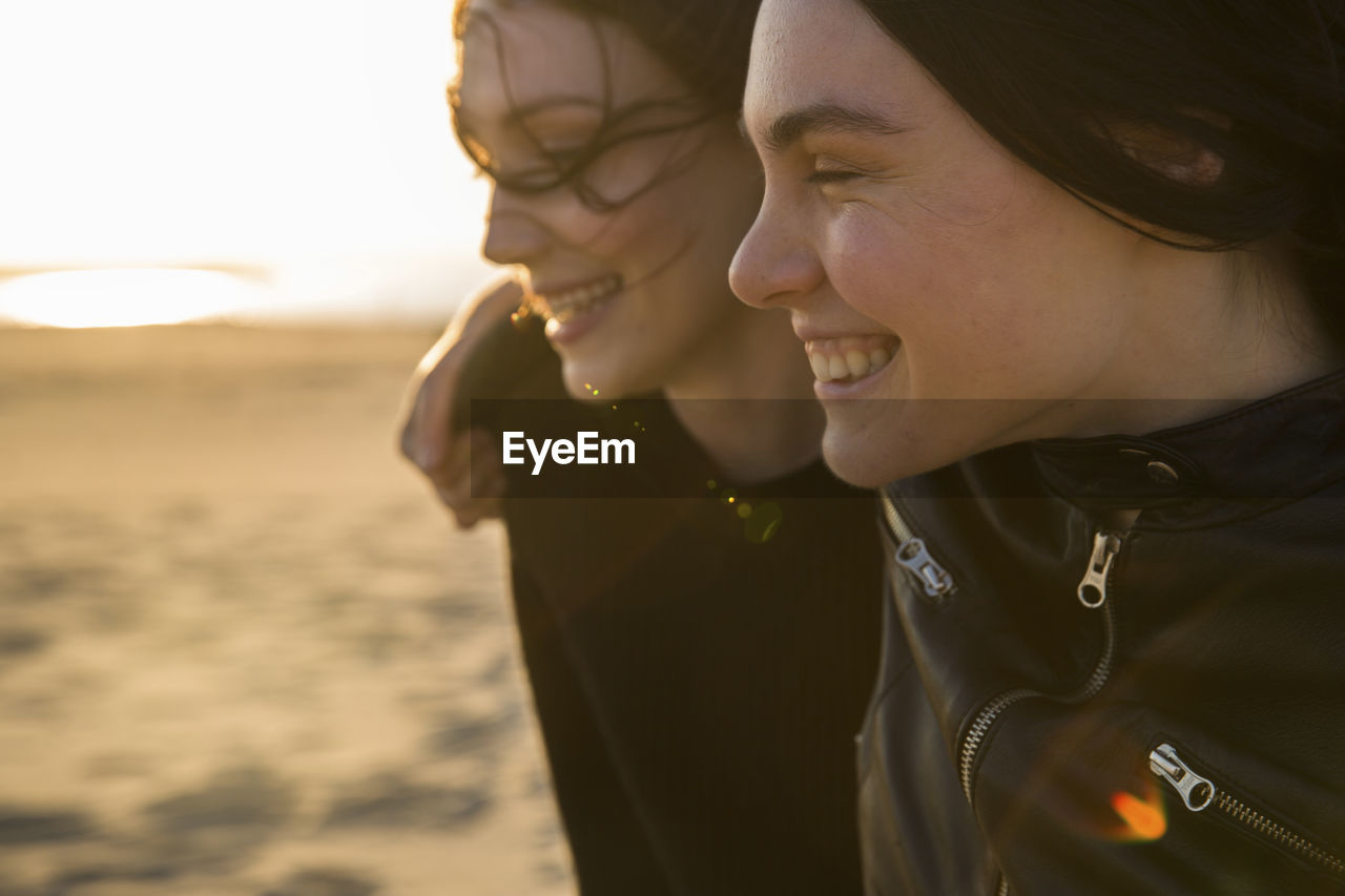 Happy female friends standing at beach during sunset