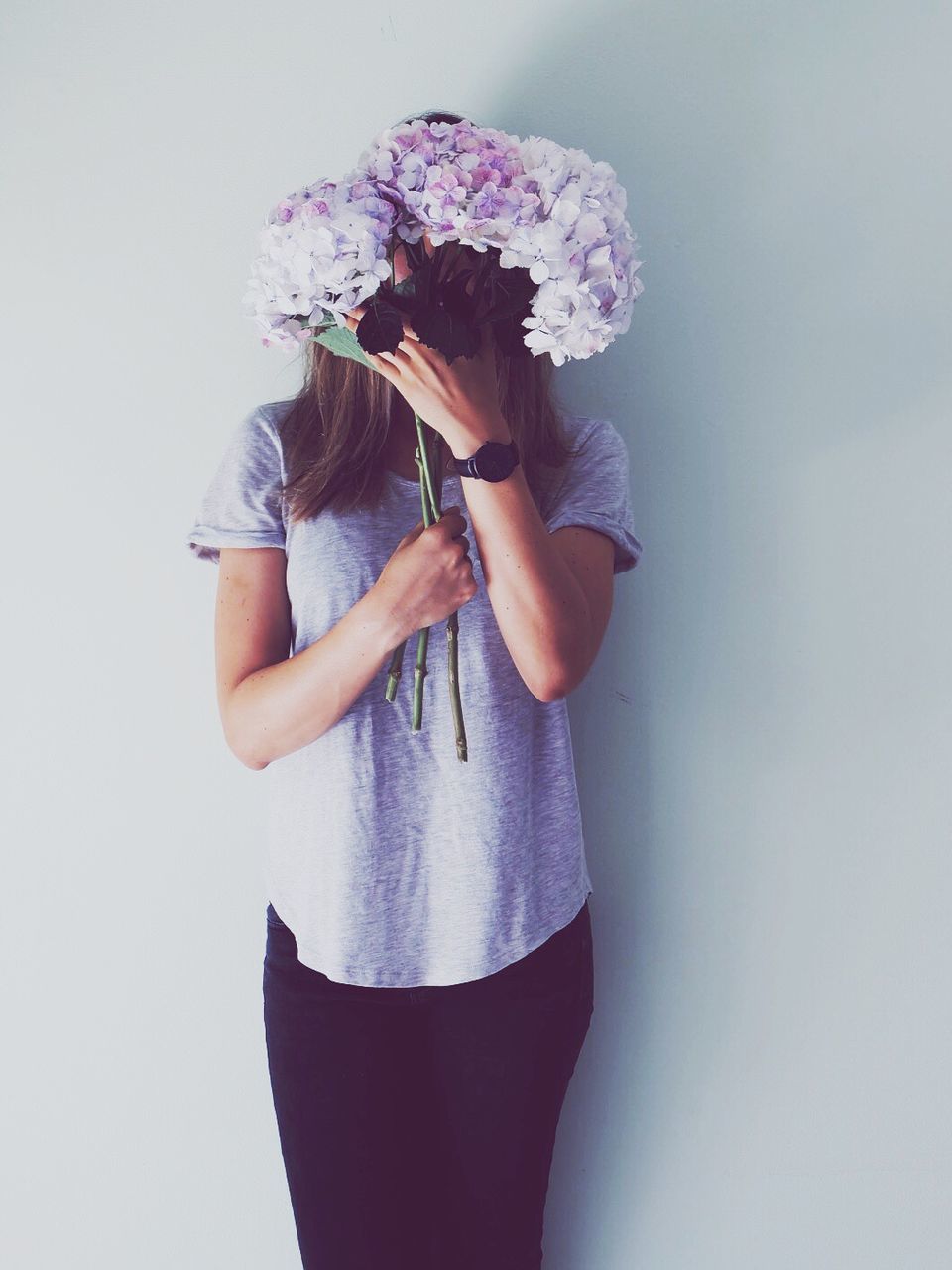 Woman covering face with flowers against white background