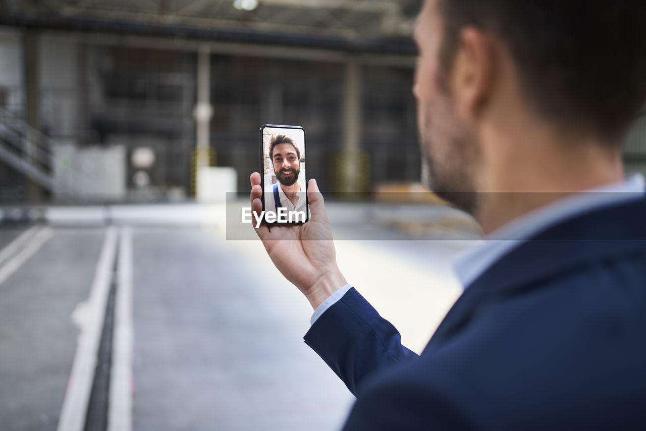 Close-up of businessman using smartphone chatting with colleague in factory