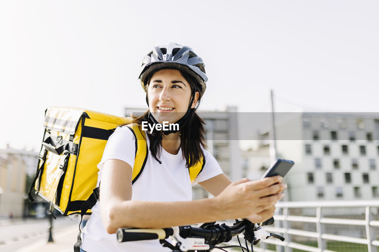 Smiling delivery woman with mobile phone leaning on bicycle handle