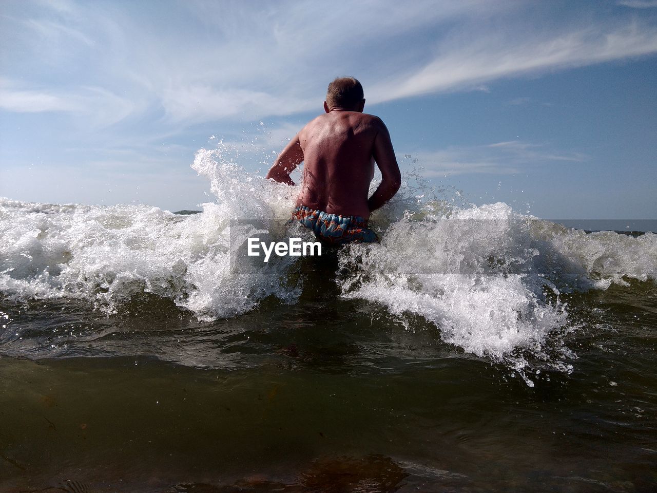 Rear view of shirtless man enjoying waves in sea against sky