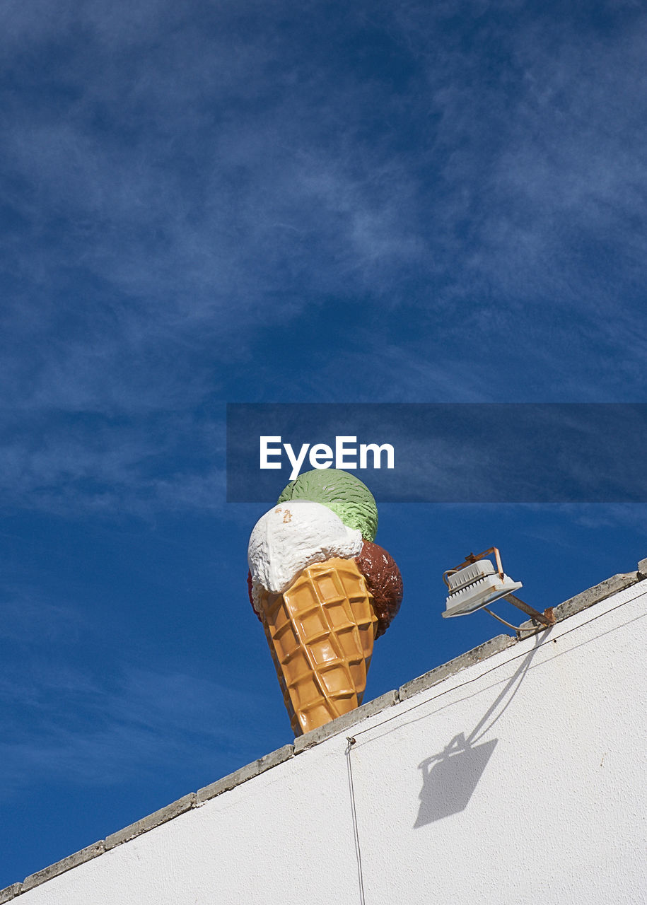 LOW ANGLE VIEW OF ICE CREAM CONE AGAINST BLUE SKY