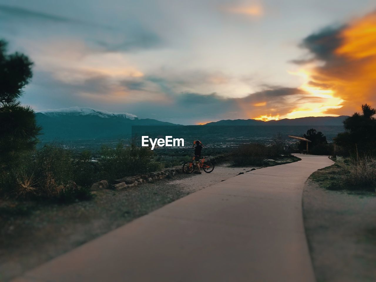 Man with bicycle on mountain against sky during sunset