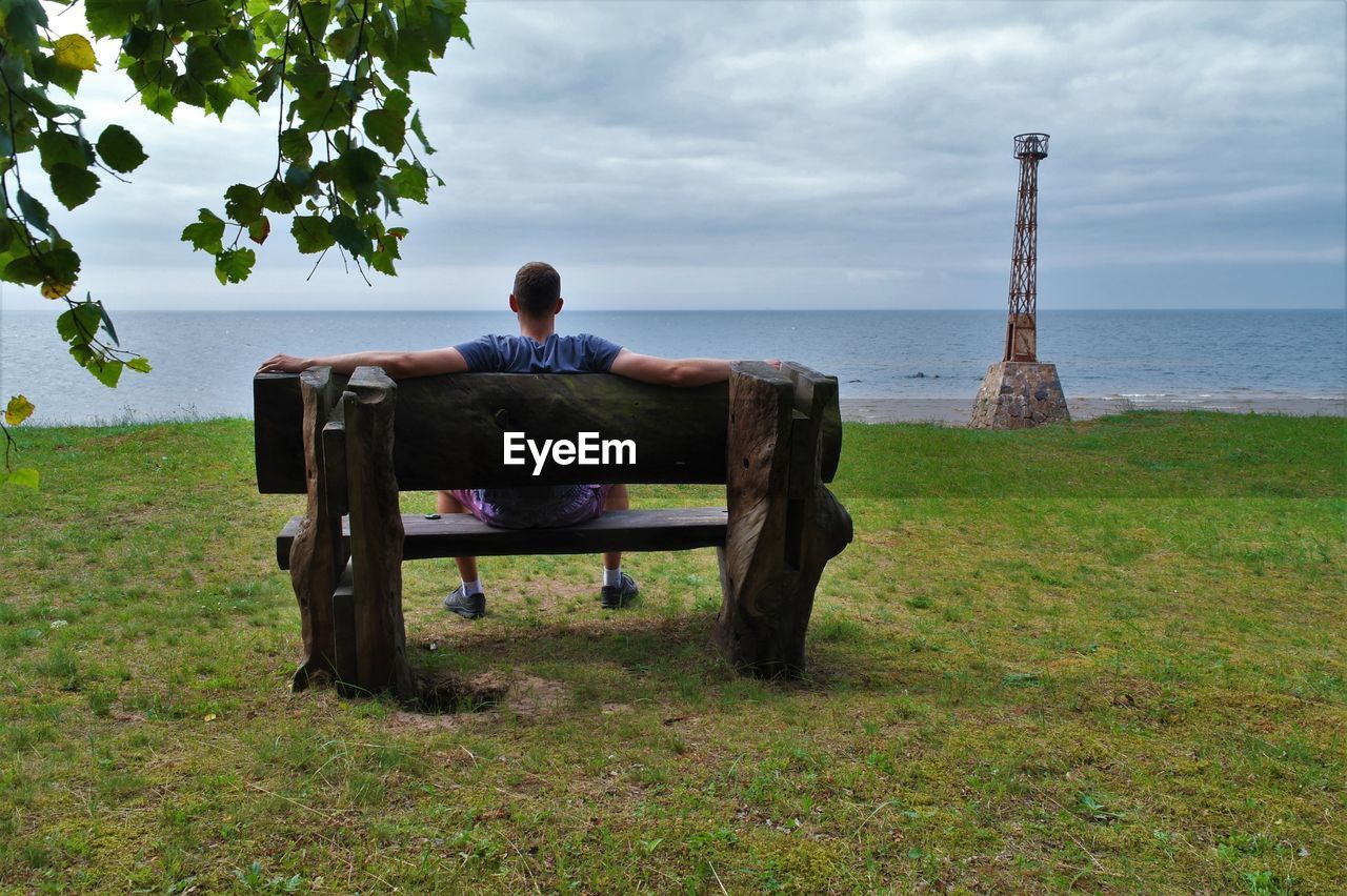 Rear view of man sitting on bench while looking at baltic sea