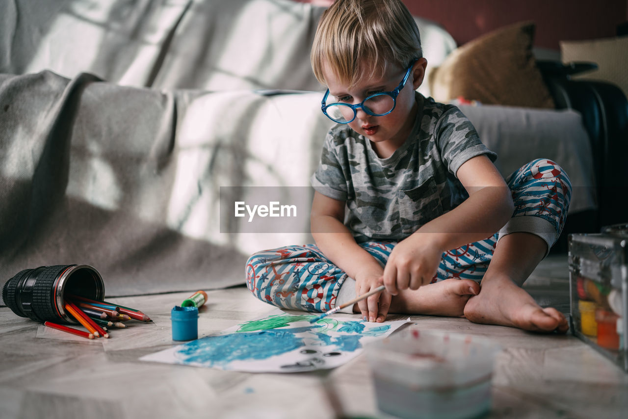 Front low angle view of child sitting on floor at home drawing