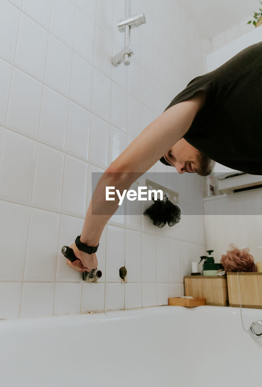 A young man repairs a faucet in the bathroom.