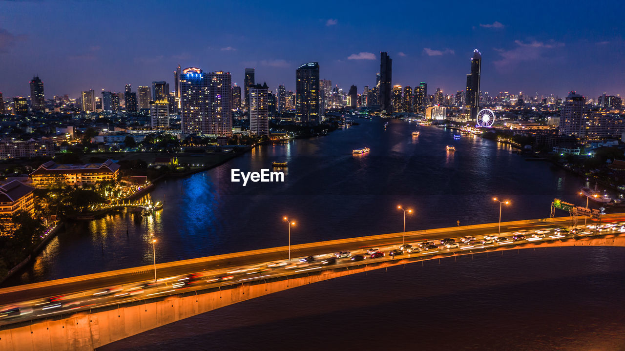 Illuminated city by river against sky at night