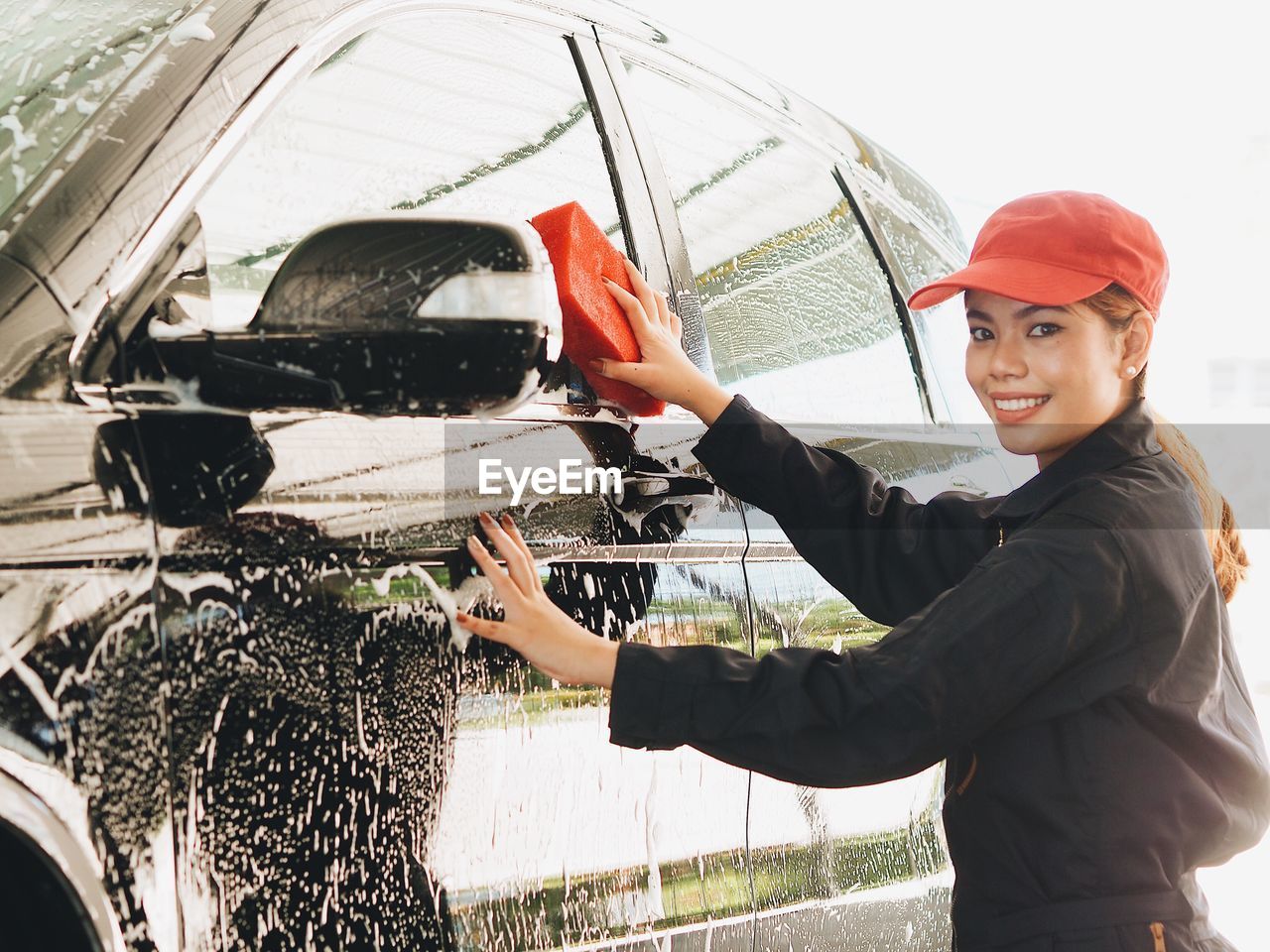 Portrait of smiling young woman cleaning car in workshop