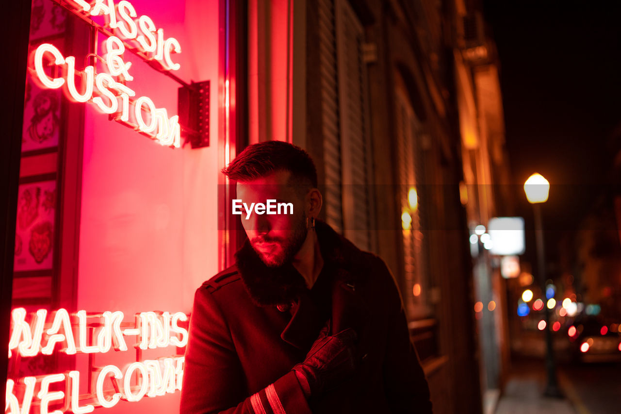 Handsome man looking down while standing by window at night