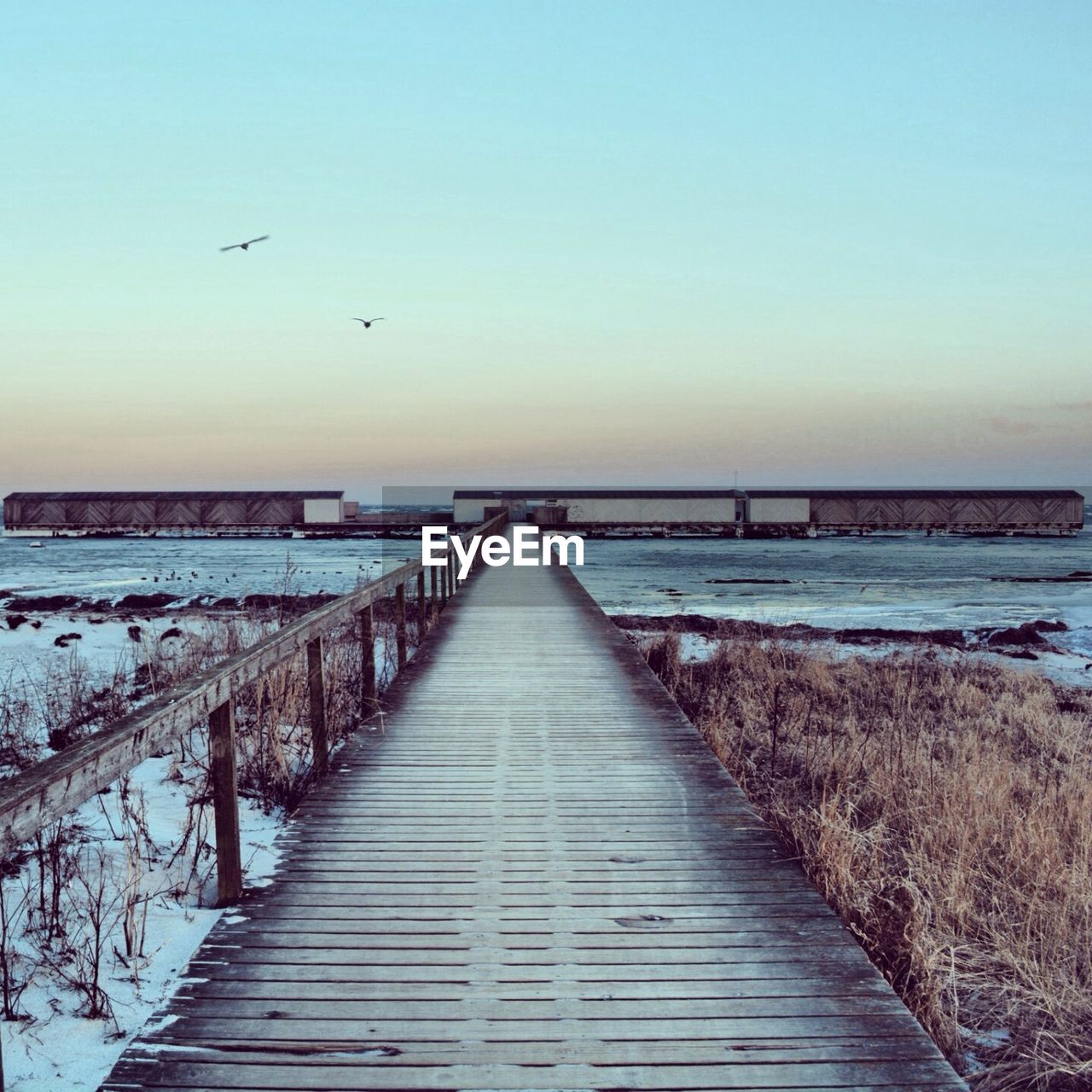 Boardwalk at river against clear sky during winter
