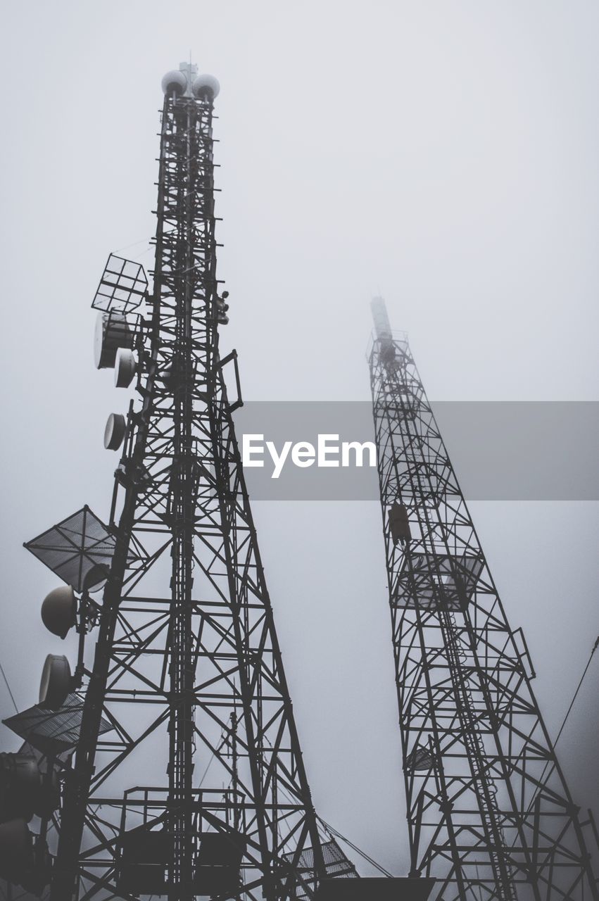 Low angle view of communications towers against sky during foggy weather