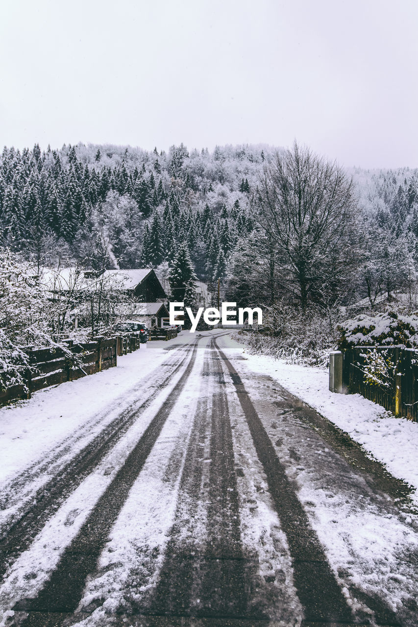 Snow covered road leading towards mountain against sky