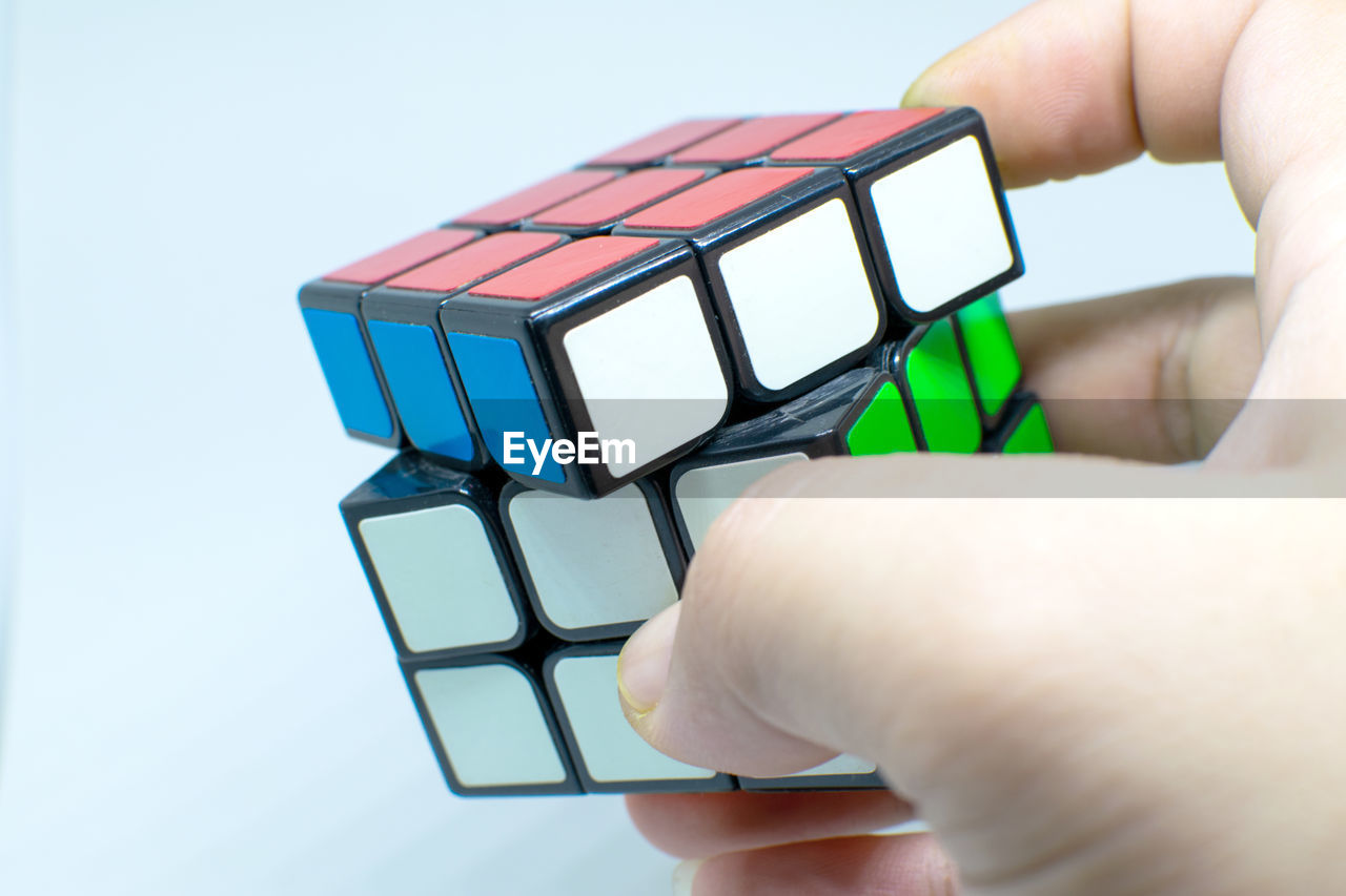 hand, rubik's cube, toy, holding, puzzle, one person, mechanical puzzle, technology, close-up, studio shot, indoors, adult, wireless technology, cube shape, computer, computer equipment, finger, business, communication