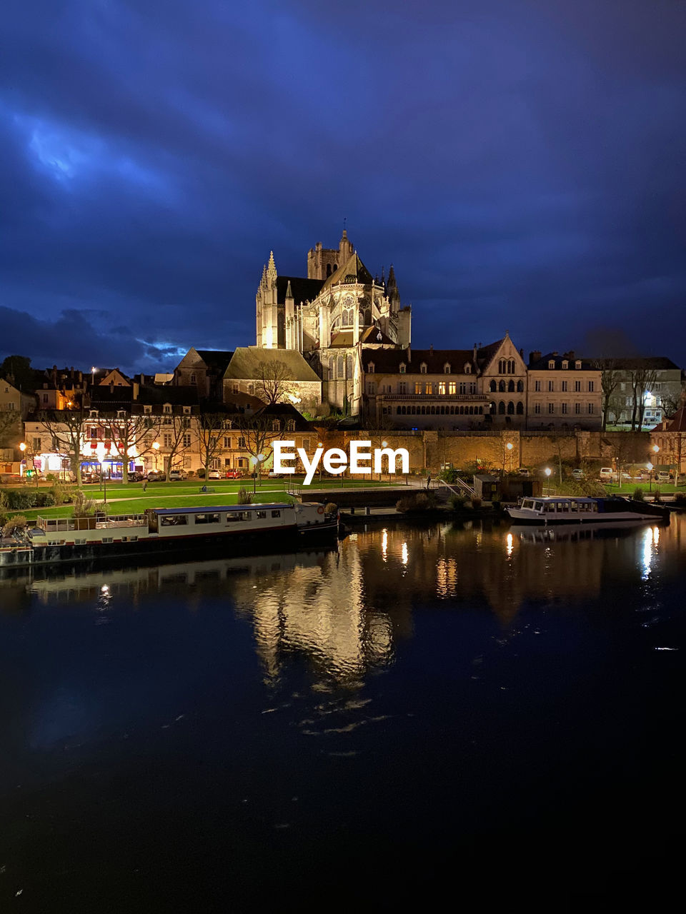 Illuminated buildings by lake against sky at night