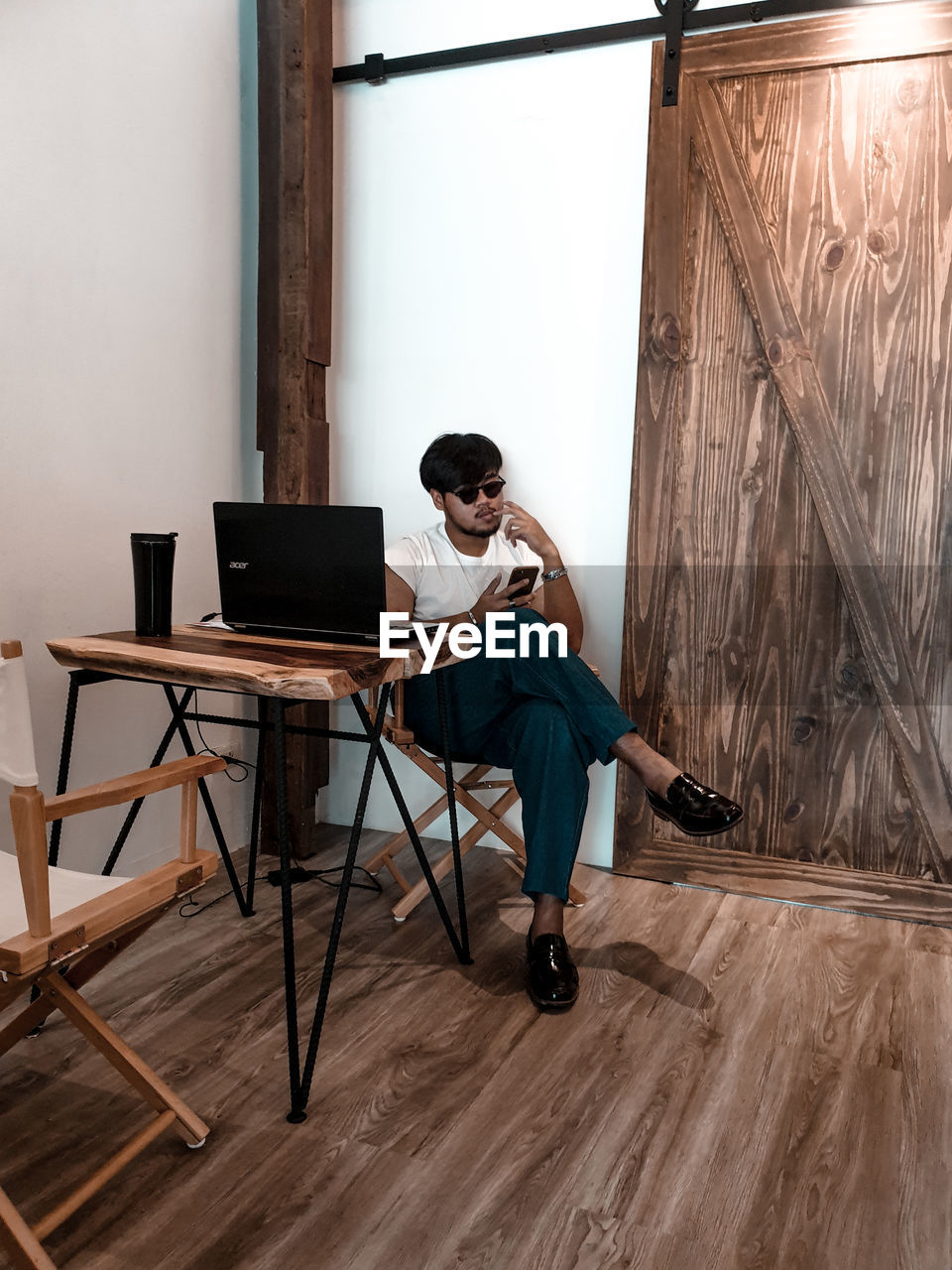 Full length of man using mobile phone while sitting on wooden table