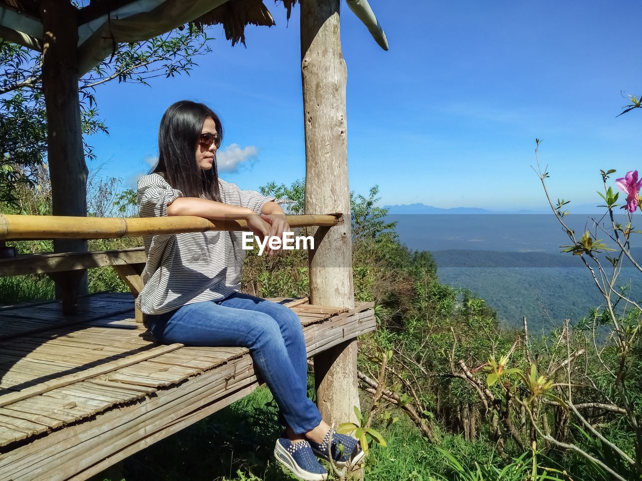 Side view of mature woman wearing sunglasses sitting on observation point against blue sky