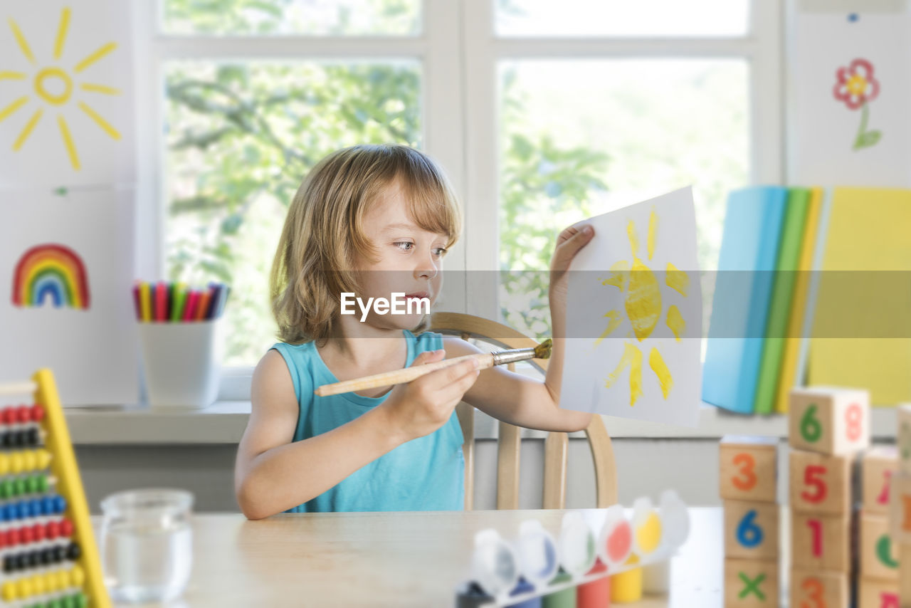 Boy painting while sitting by table